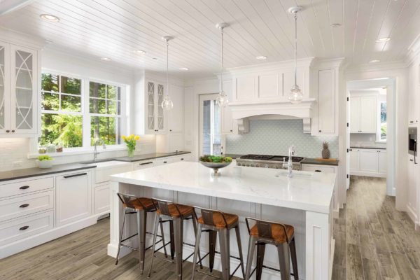 White Kitchen Interior with Island, Sink, Cabinets, and Hardwood Floors in New Luxury Home with Lights On