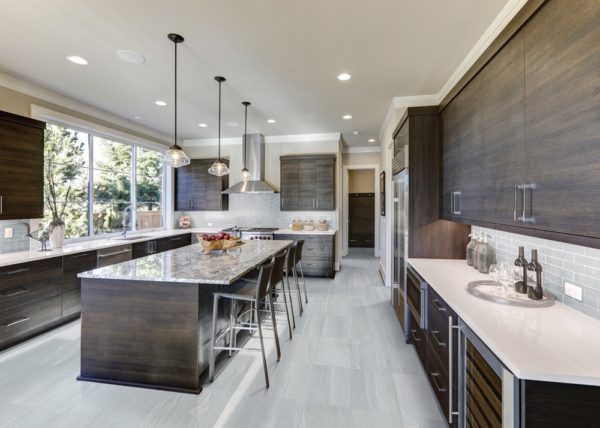 Modern gray kitchen features dark gray flat front cabinets paired with white quartz countertops and a glossy gray linear tile backsplash. Bar style kitchen island with granite counter. Northwest, USA