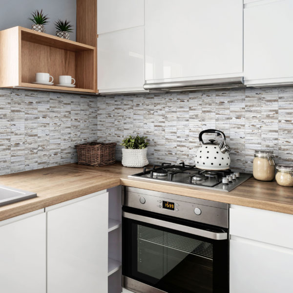 Small white kitchen with stylish tiles, wooden cabinets and sink with faucet near the window. Scandinavian interior of room in apartment.